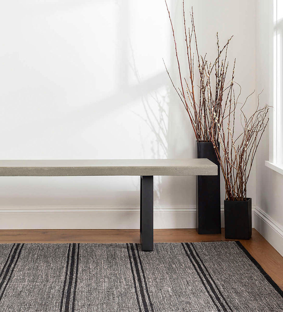 Malta Black Woven Wool Rug displayed with a bench and two planters.