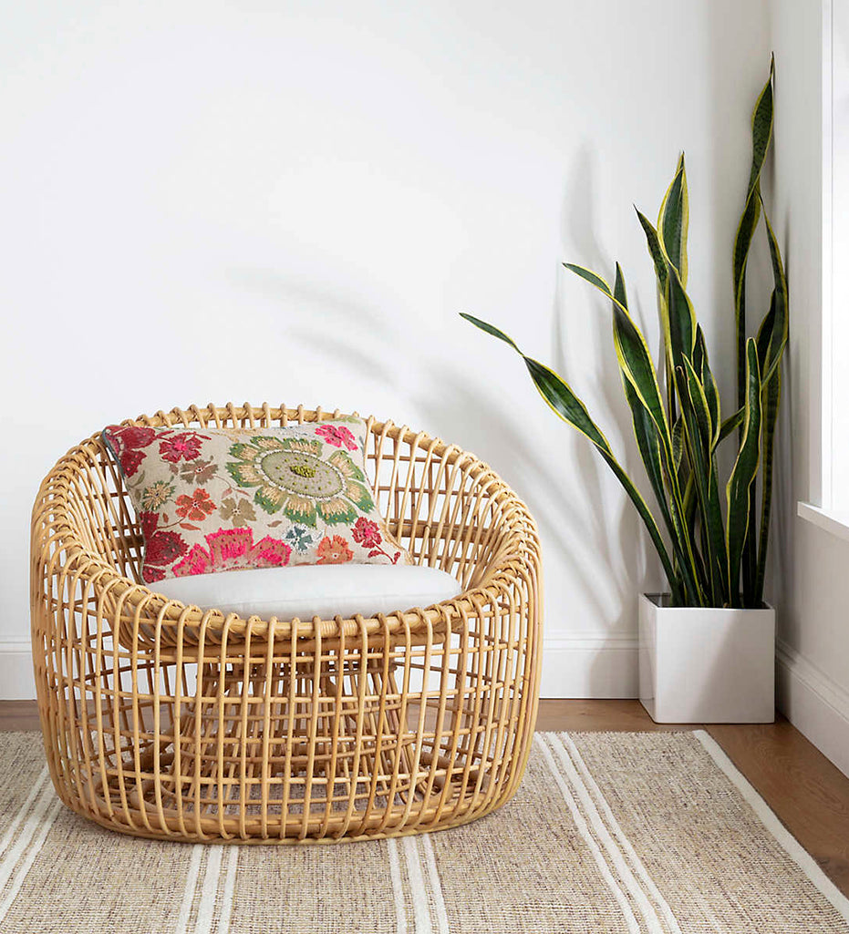 Malta Natural Woven Wool Rug displayed with a lounge chair, throw pillow, and plant. 