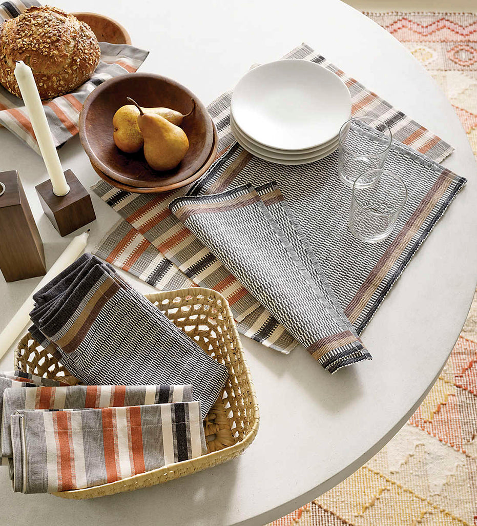 A beautiful tabletop display including: Ethan Stripe Napkins, Ethan Stripe Placemats, plates, water glasses, candles, a loaf of bread, and a bowl of pears.